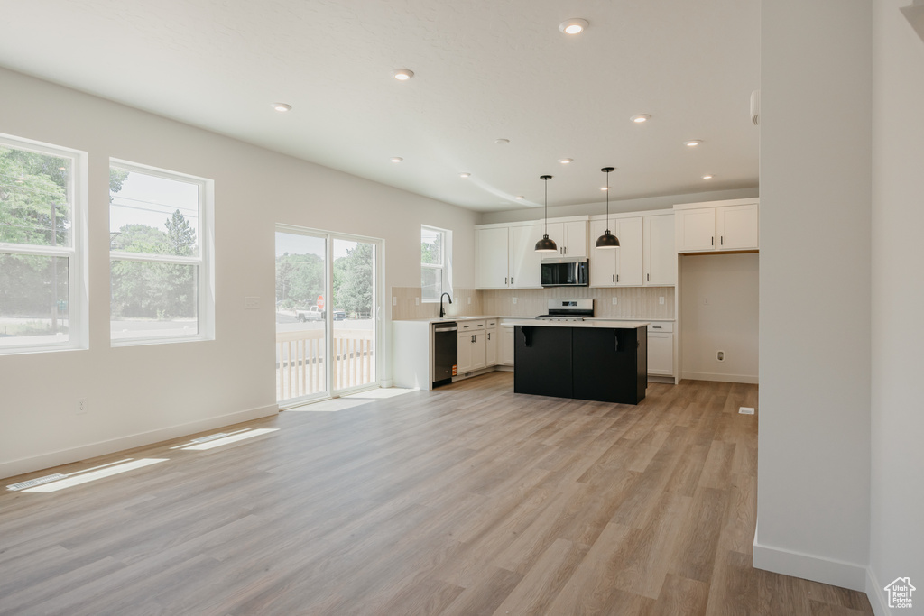 Kitchen with appliances with stainless steel finishes, white cabinetry, tasteful backsplash, light countertops, and a center island