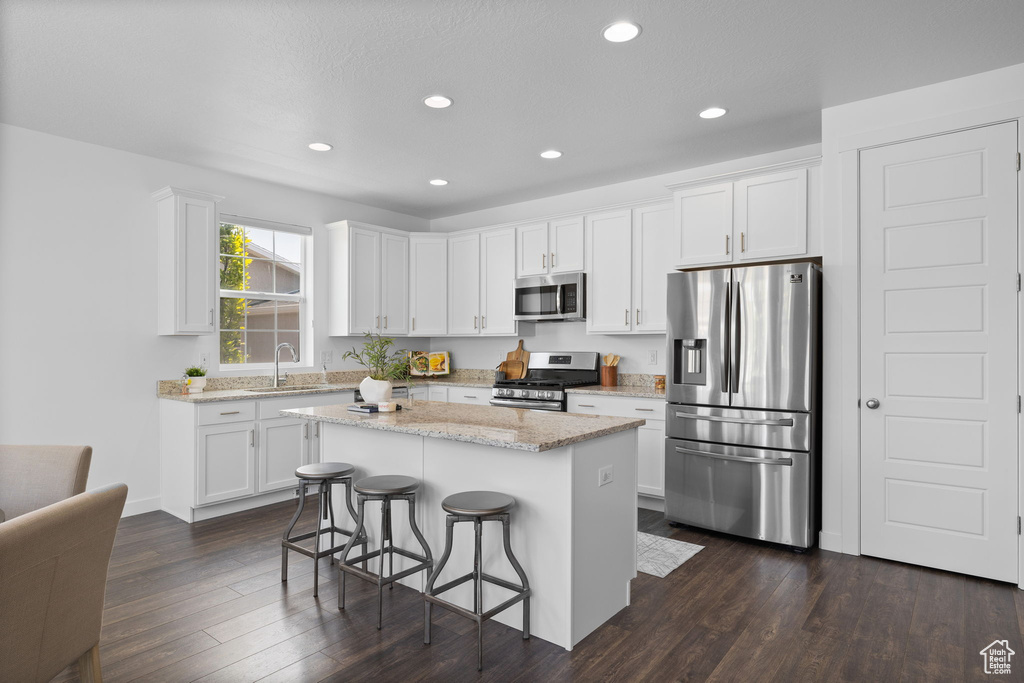Kitchen featuring stainless steel appliances, white cabinets, a kitchen breakfast bar, dark wood-type flooring, and recessed lighting