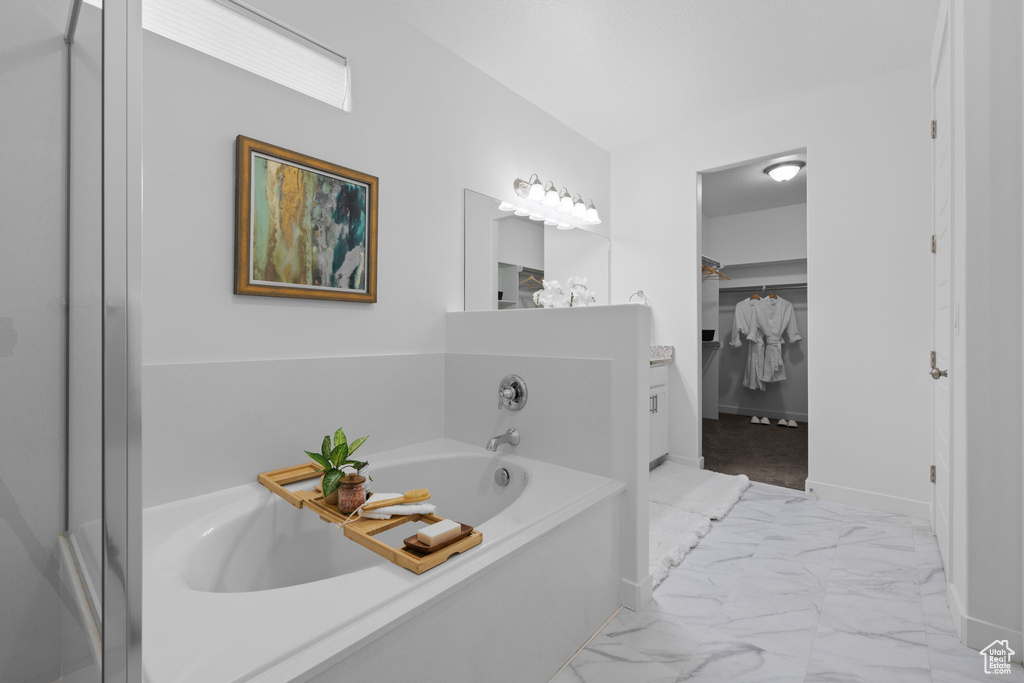 Full bathroom with marble look tile flooring, a bath, and a spacious closet