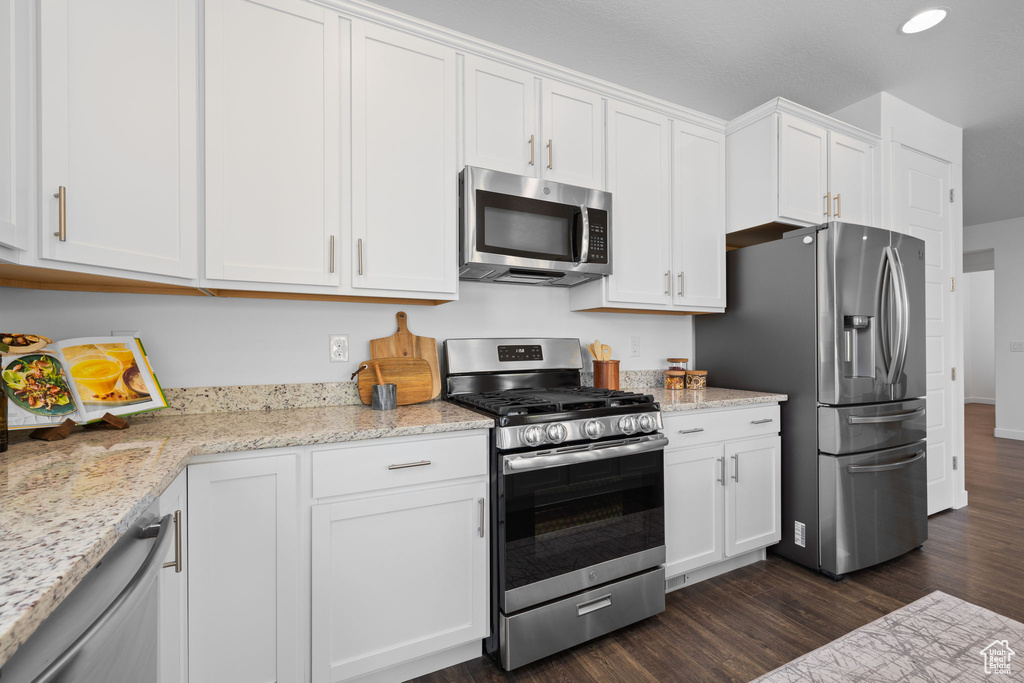 Kitchen with stainless steel appliances, dark wood finished floors, white cabinetry, and light stone counters