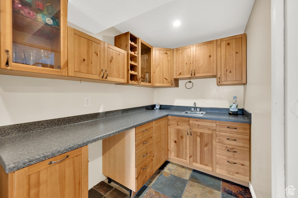 Kitchen featuring dark countertops, dark stone finish floors, glass insert cabinets, and light brown cabinets