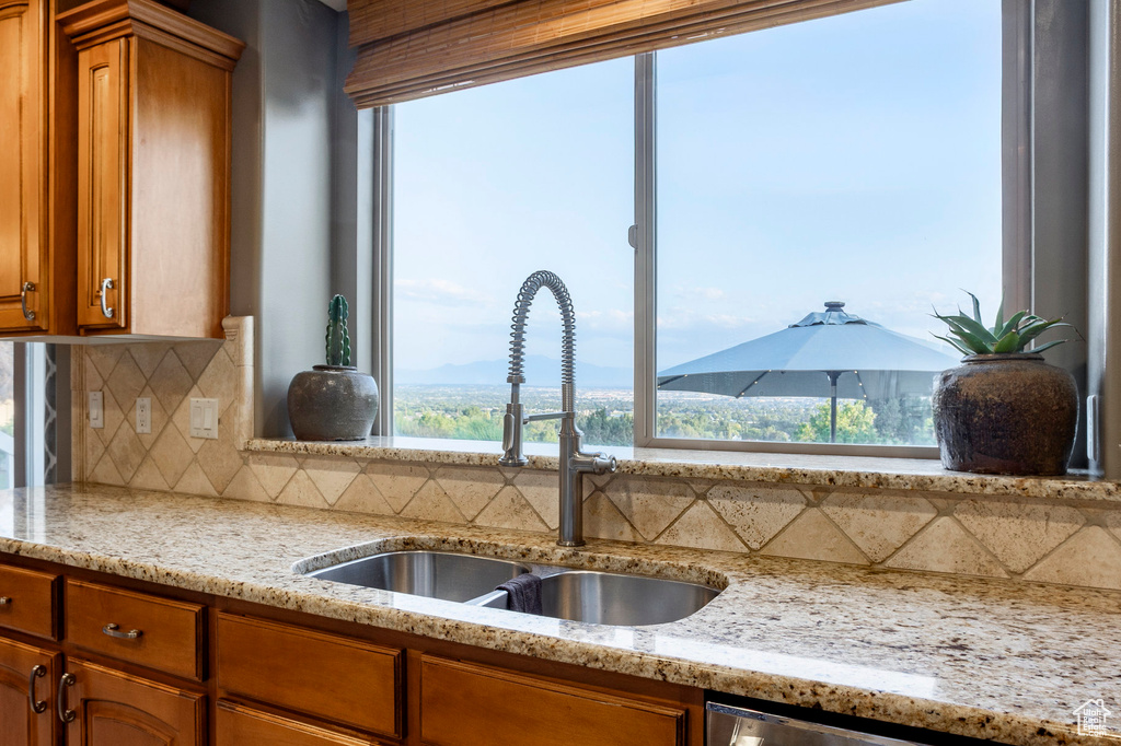Kitchen featuring brown cabinetry, backsplash, and light stone counters