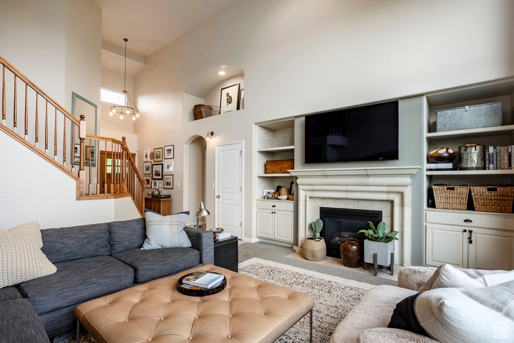 Living room with a towering ceiling, stairway, carpet flooring, built in shelves, and a tile fireplace