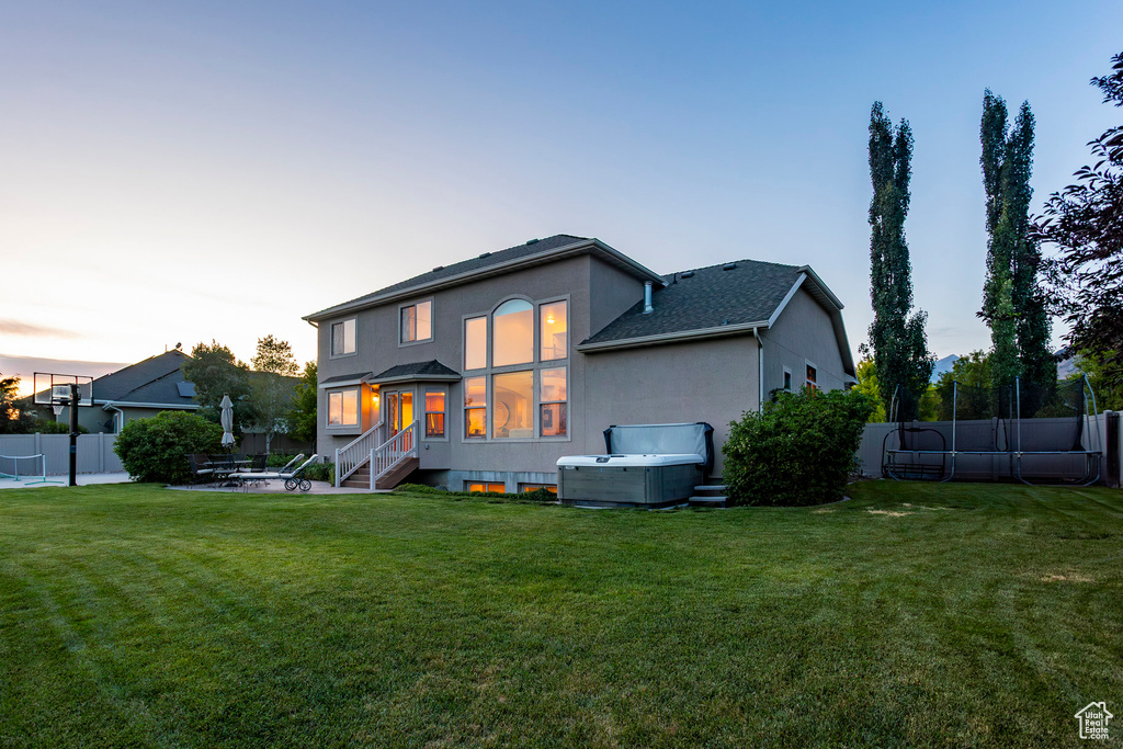 Back of property at dusk featuring a hot tub, stucco siding, and a patio area