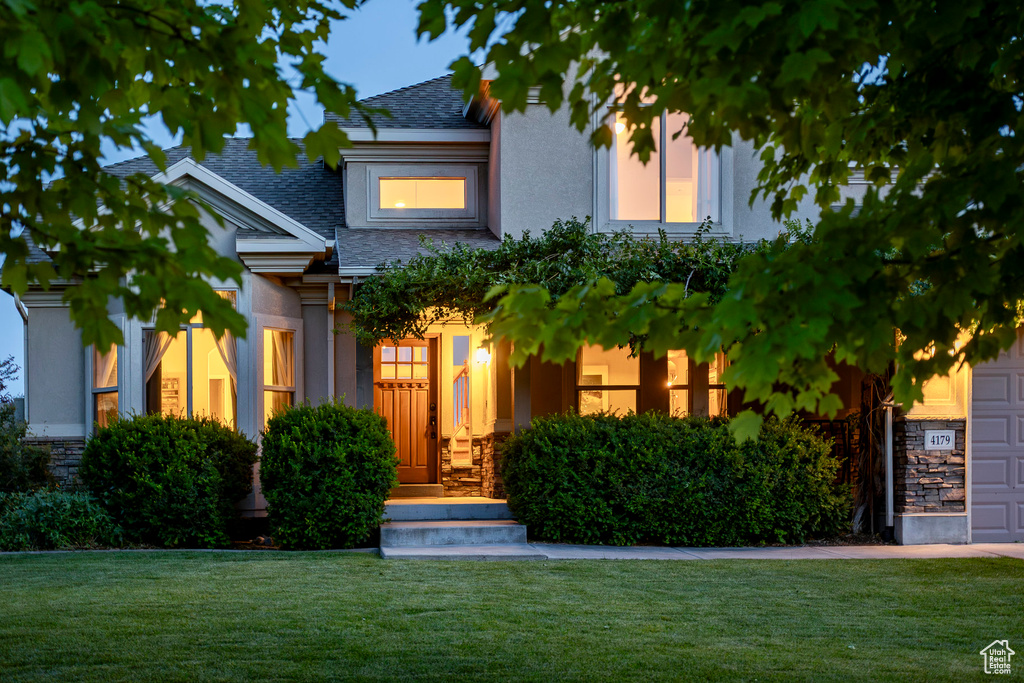 View of front facade featuring a front yard, a shingled roof, stucco siding, and stone siding