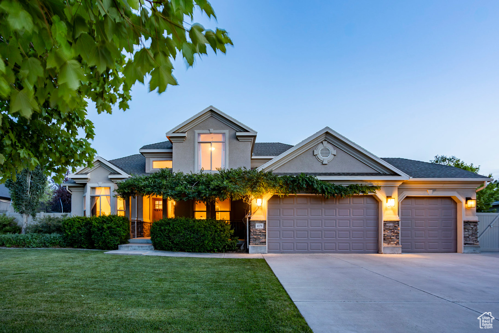 View of front facade featuring an attached garage, stone siding, driveway, and a front yard