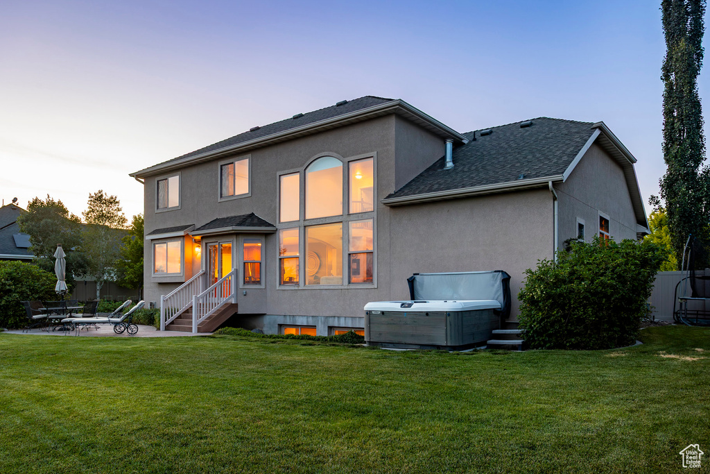 Back of house with stucco siding, a patio, a hot tub, and a shingled roof