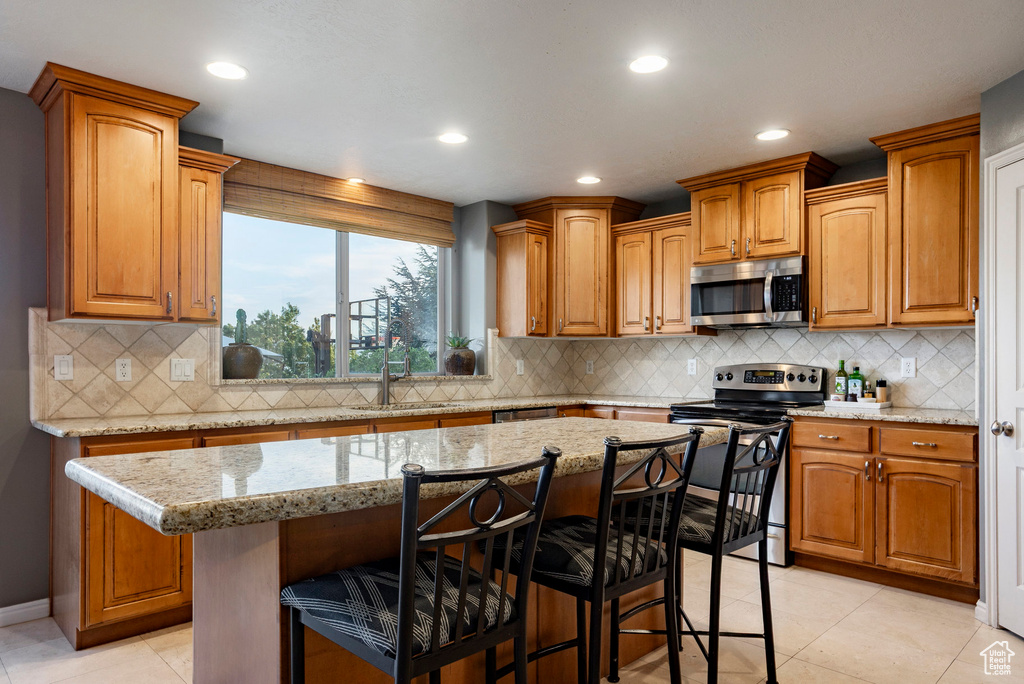 Kitchen with appliances with stainless steel finishes, a breakfast bar area, backsplash, recessed lighting, and light stone counters