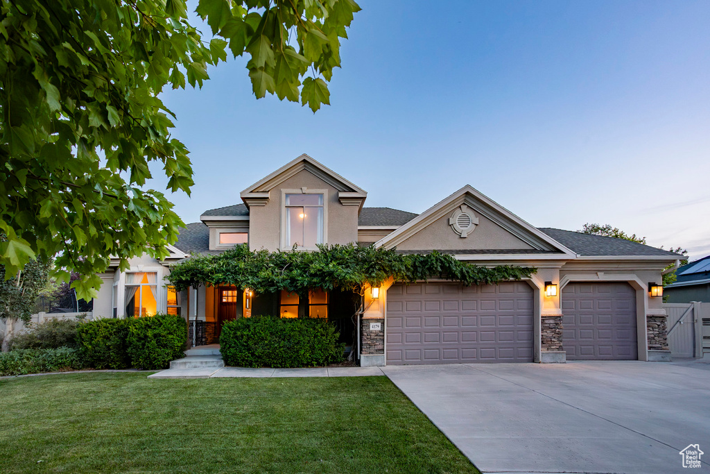 View of front of home with stucco siding, stone siding, a front yard, and driveway