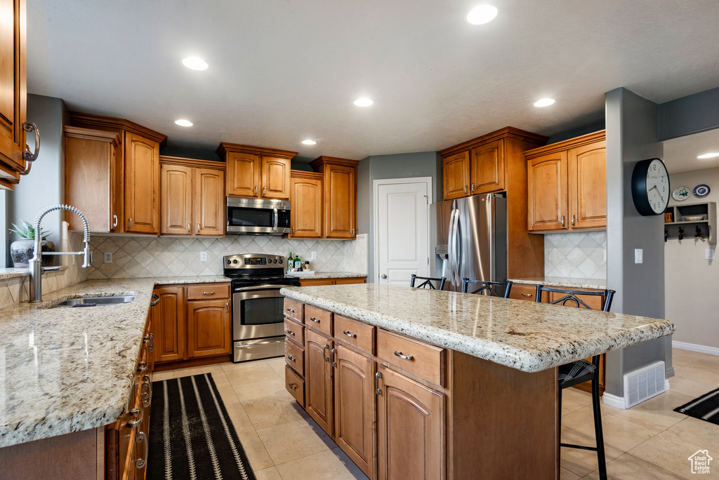 Kitchen featuring stainless steel appliances, a center island, a kitchen bar, tasteful backsplash, and light stone counters