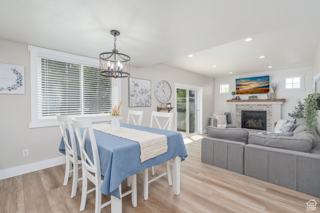 Dining area with a chandelier, light wood-type flooring, plenty of natural light, recessed lighting, and a brick fireplace