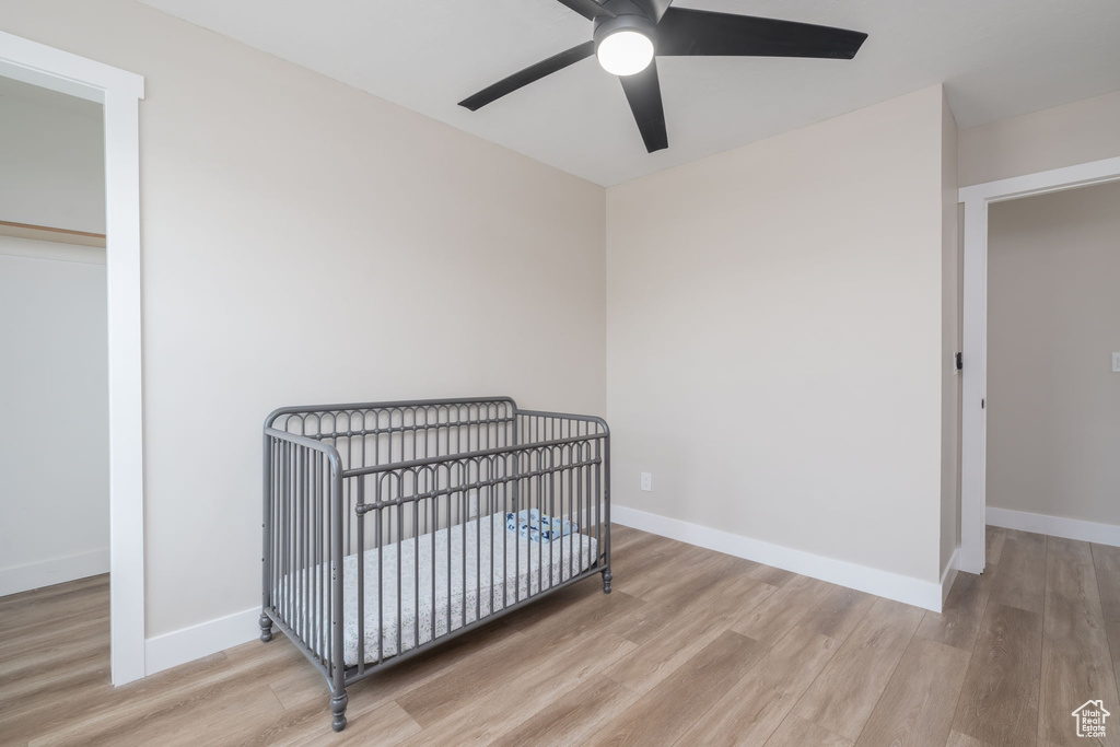 Bedroom featuring wood finished floors, a nursery area, and ceiling fan