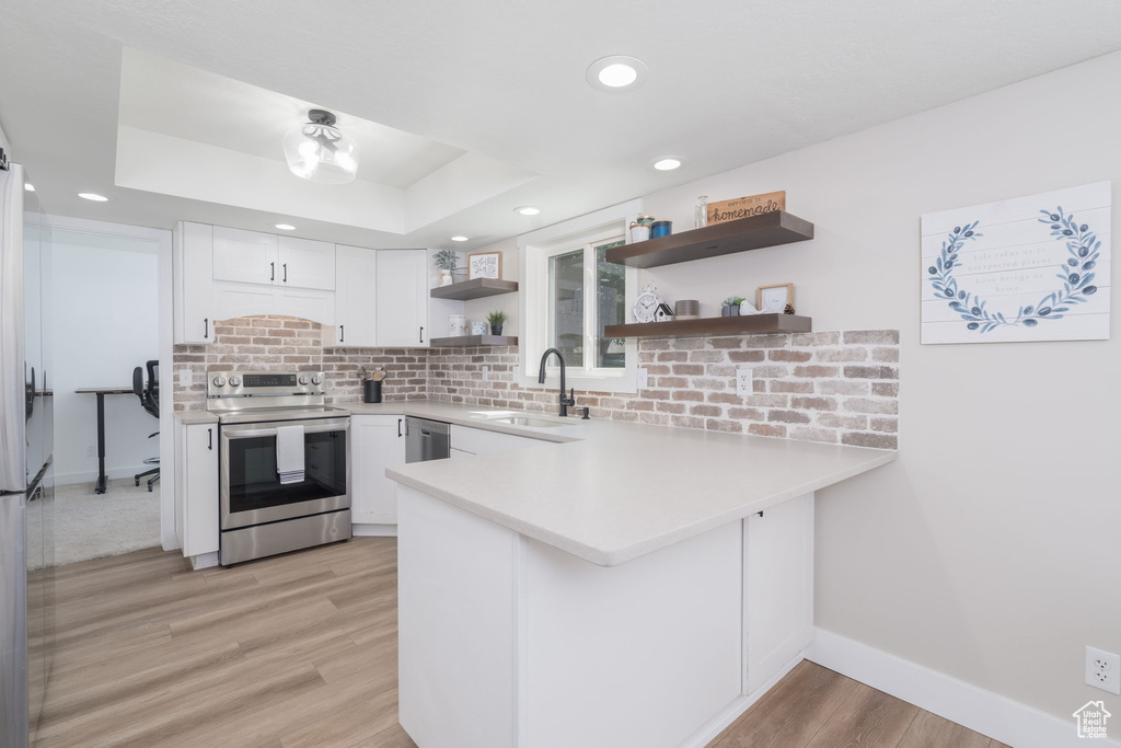 Kitchen featuring appliances with stainless steel finishes, open shelves, light wood-type flooring, a peninsula, and white cabinetry