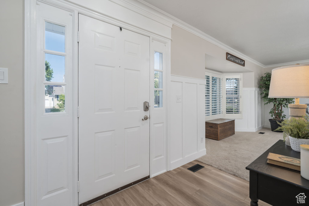 Entryway with crown molding, wood finished floors, wainscoting, and a decorative wall