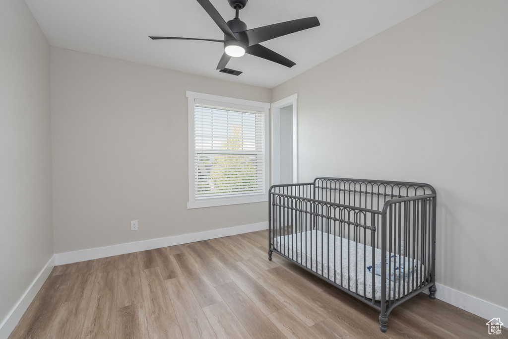 Bedroom with wood finished floors, a ceiling fan, and a crib