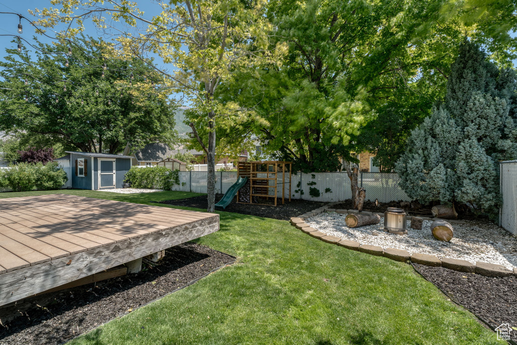 Fenced backyard with a playground, a shed, and a deck