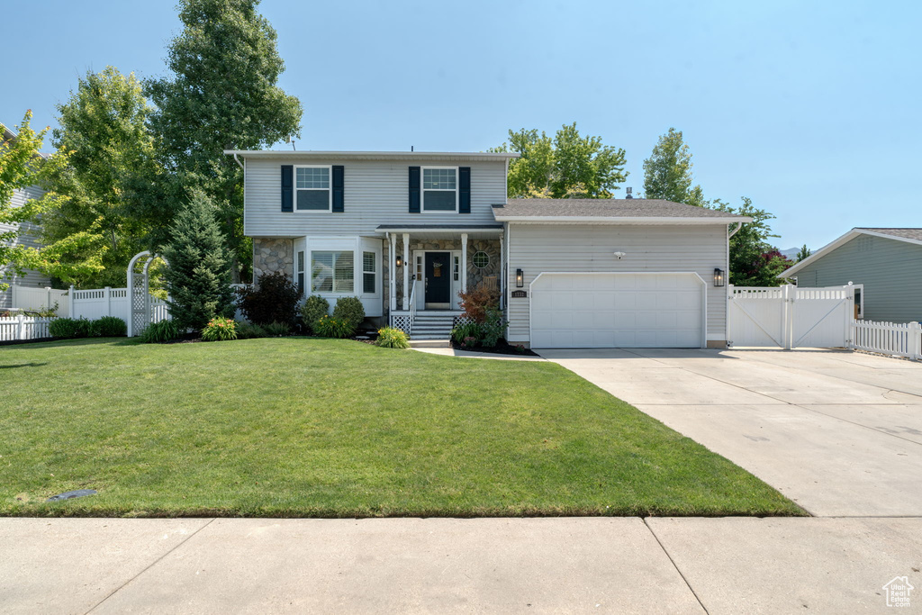 Traditional-style home featuring an attached garage, a gate, concrete driveway, and stone siding