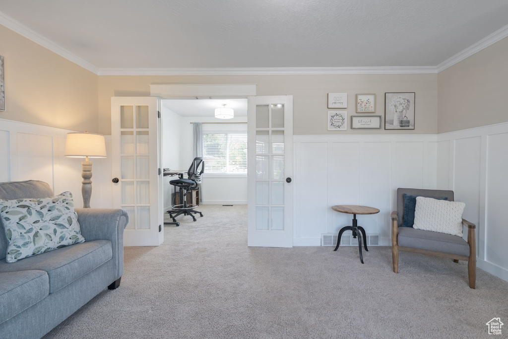 Living area with french doors, crown molding, carpet, a decorative wall, and a wainscoted wall