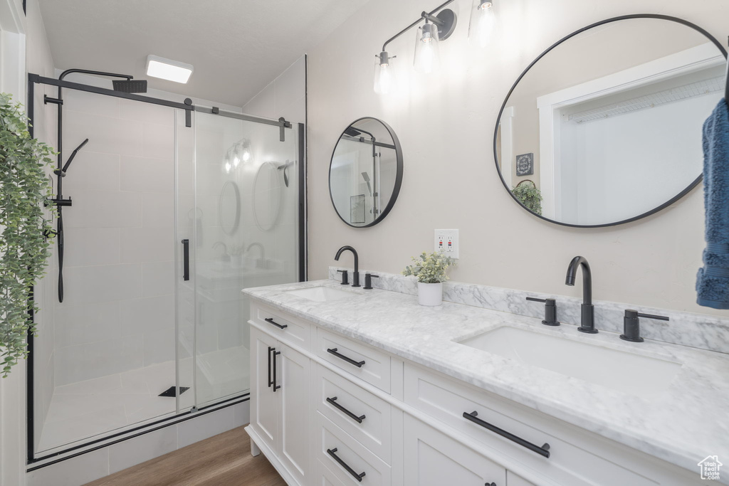 Bathroom featuring double vanity, a shower stall, and wood finished floors