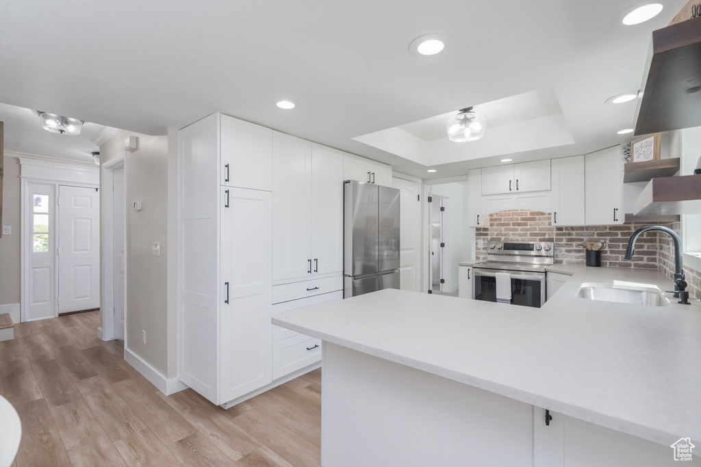 Kitchen featuring stainless steel appliances, light countertops, light wood-type flooring, backsplash, and a peninsula