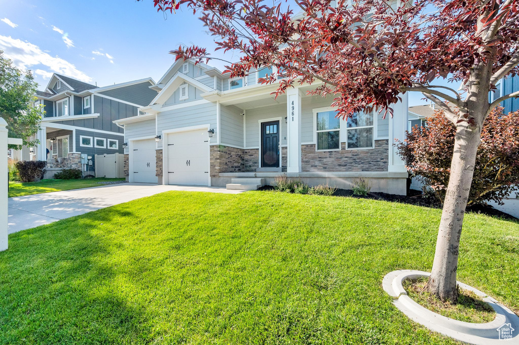 View of front of house featuring board and batten siding, stone siding, a front lawn, and driveway