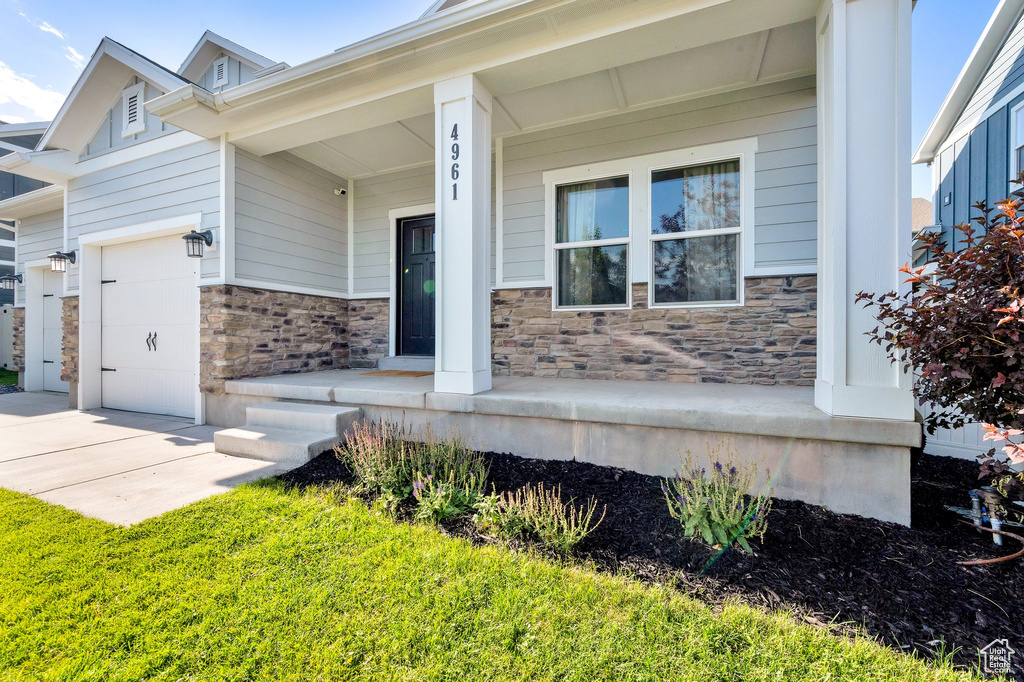 View of front of property featuring stone siding, a garage, and a porch
