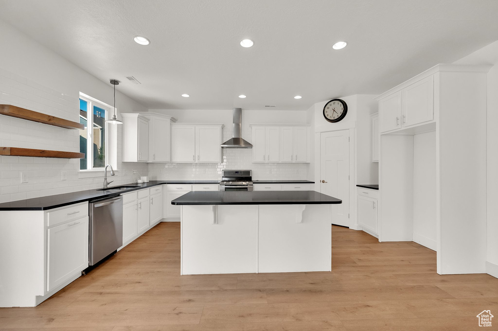 Kitchen with stainless steel appliances, wall chimney exhaust hood, dark countertops, a center island, and tasteful backsplash