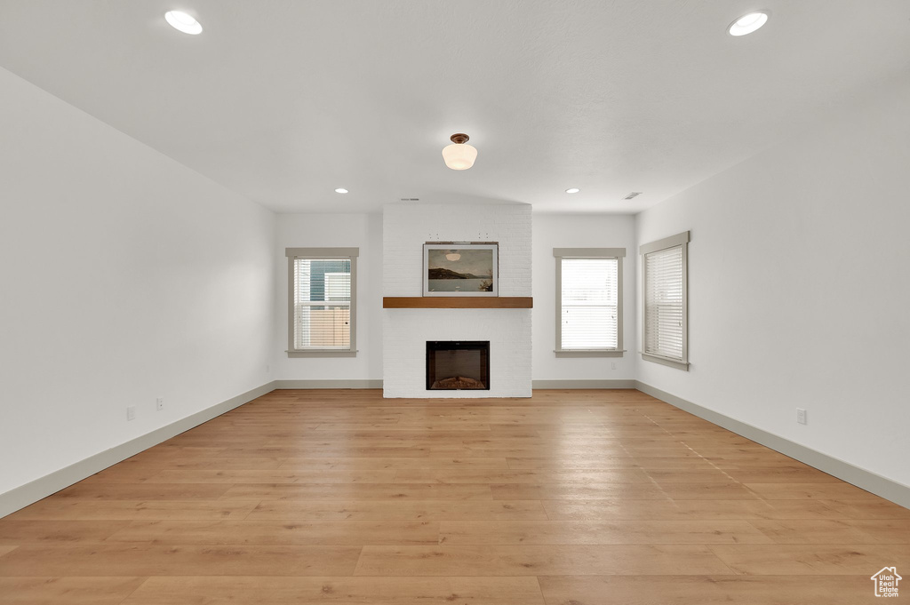 Unfurnished living room with healthy amount of natural light, recessed lighting, a fireplace, and light wood-style flooring