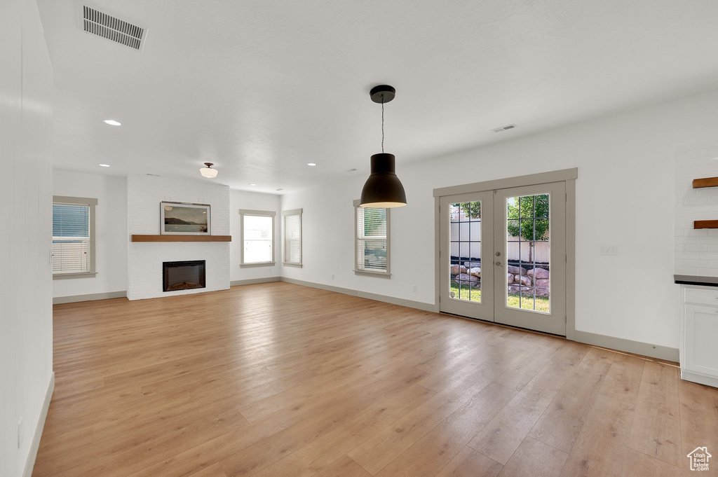 Unfurnished living room featuring plenty of natural light, light wood-type flooring, a large fireplace, recessed lighting, and french doors