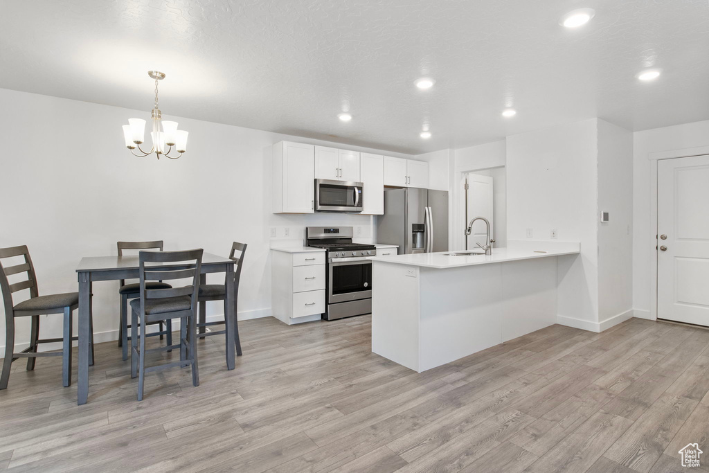Kitchen with appliances with stainless steel finishes, light wood-style flooring, a peninsula, a chandelier, and white cabinets