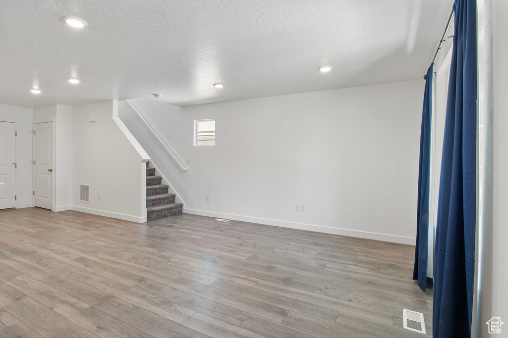 Unfurnished living room featuring stairway, wood finished floors, recessed lighting, and a textured ceiling