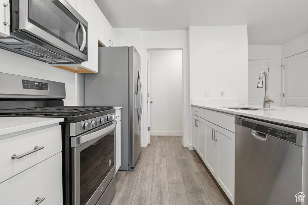 Kitchen featuring appliances with stainless steel finishes, light wood-style floors, white cabinetry, and light countertops