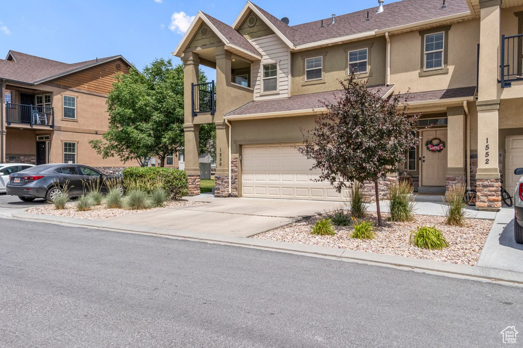 View of property with stucco siding, an attached garage, concrete driveway, and stone siding