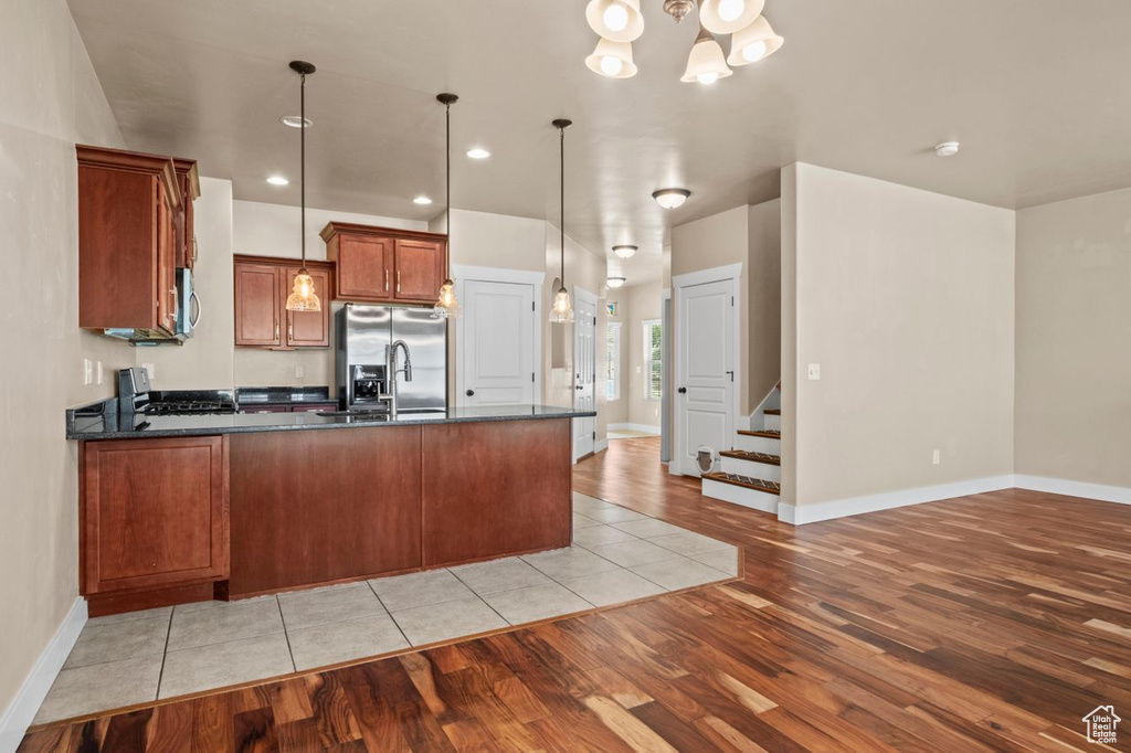 Kitchen with appliances with stainless steel finishes, light wood-style floors, a peninsula, brown cabinetry, and hanging light fixtures