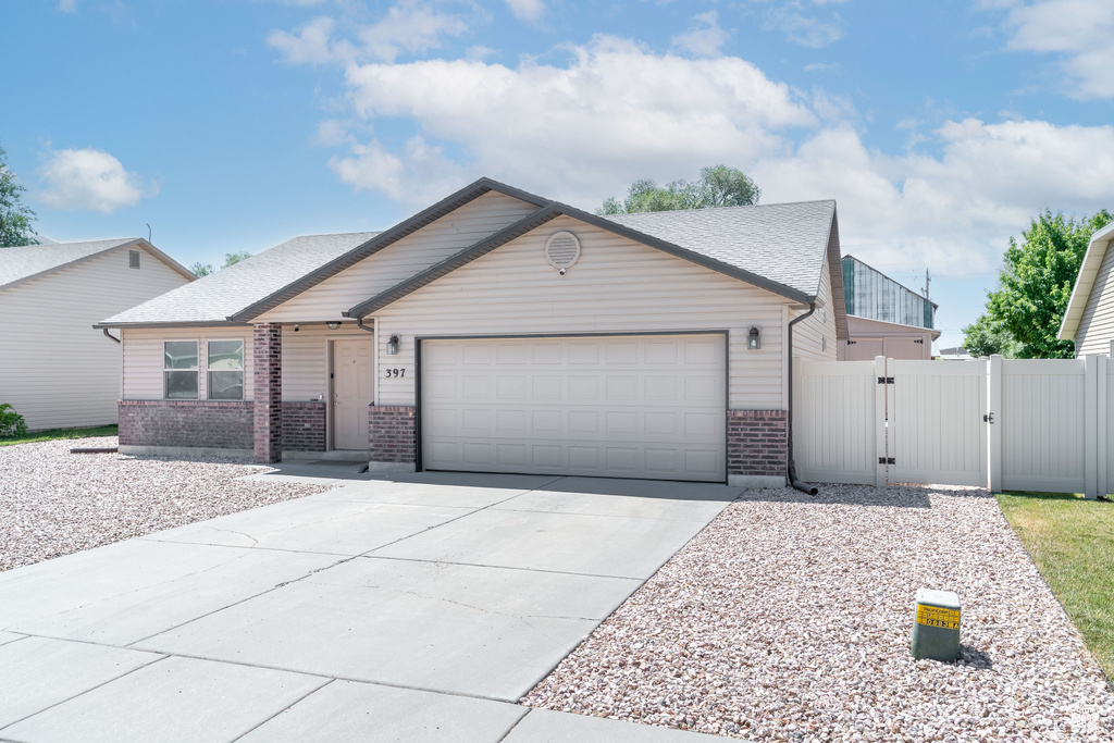 View of front facade with a gate, brick siding, a garage, driveway, and a shingled roof
