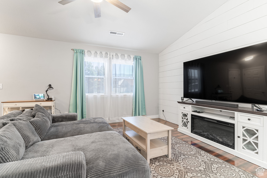 Living room with vaulted ceiling, wooden walls, wood finished floors, and a ceiling fan