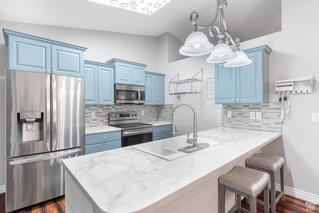 Kitchen featuring stainless steel appliances, blue cabinets, a breakfast bar area, vaulted ceiling, and a peninsula