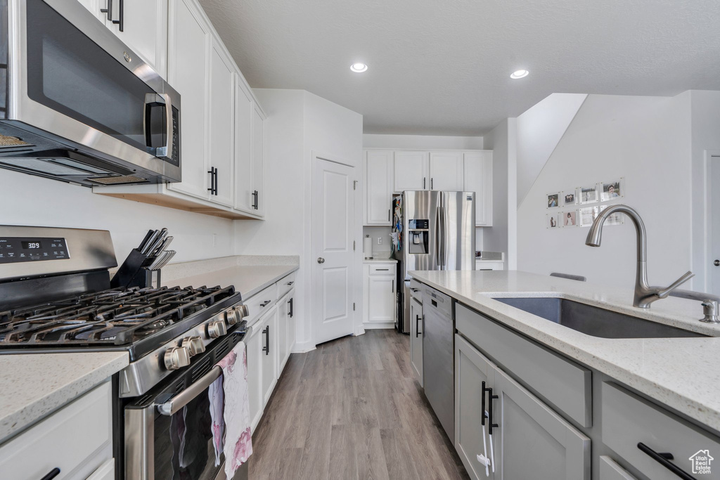 Kitchen with appliances with stainless steel finishes, light wood-style floors, light stone counters, white cabinets, and recessed lighting