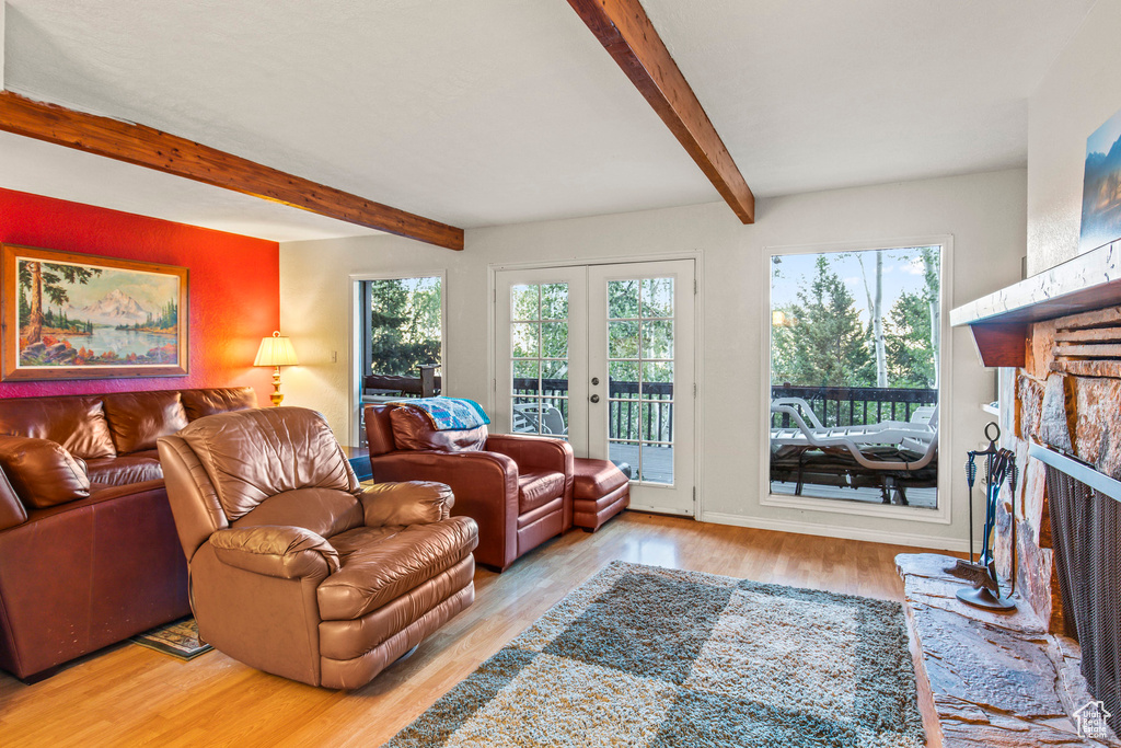 Living area featuring a fireplace with raised hearth, beam ceiling, wood finished floors, and french doors
