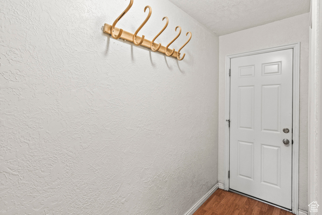 Doorway with dark wood-type flooring, a textured ceiling, and a textured wall