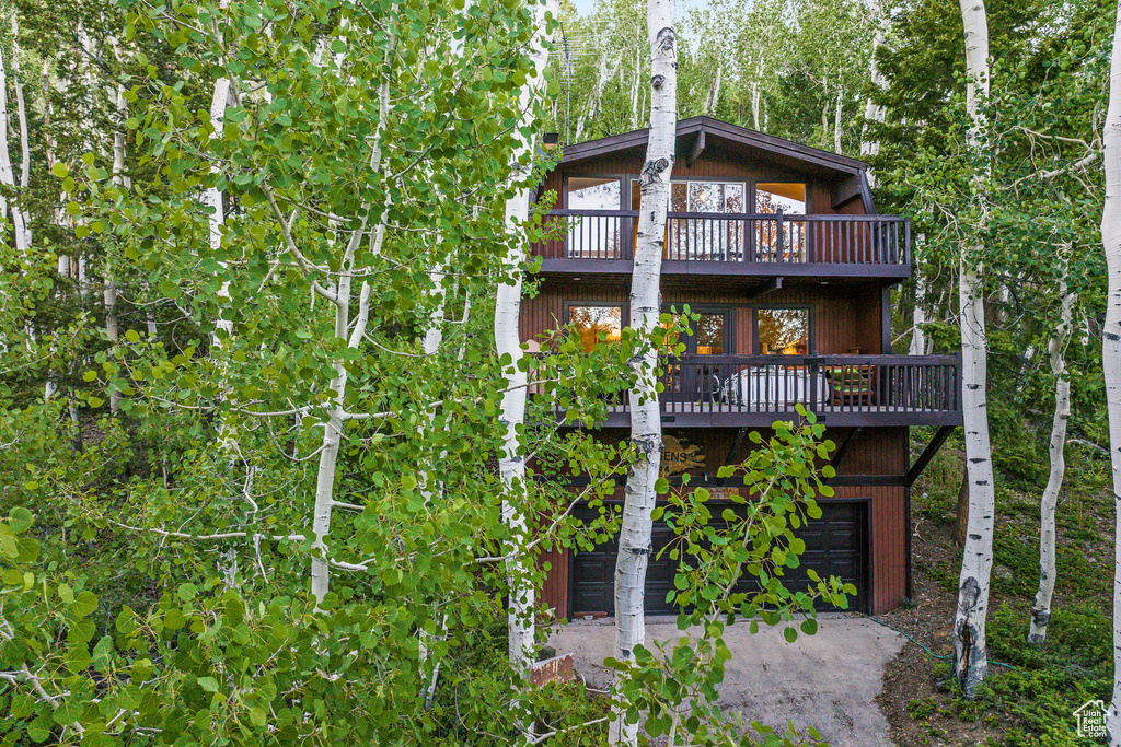 Back of house featuring a balcony, an attached garage, and driveway