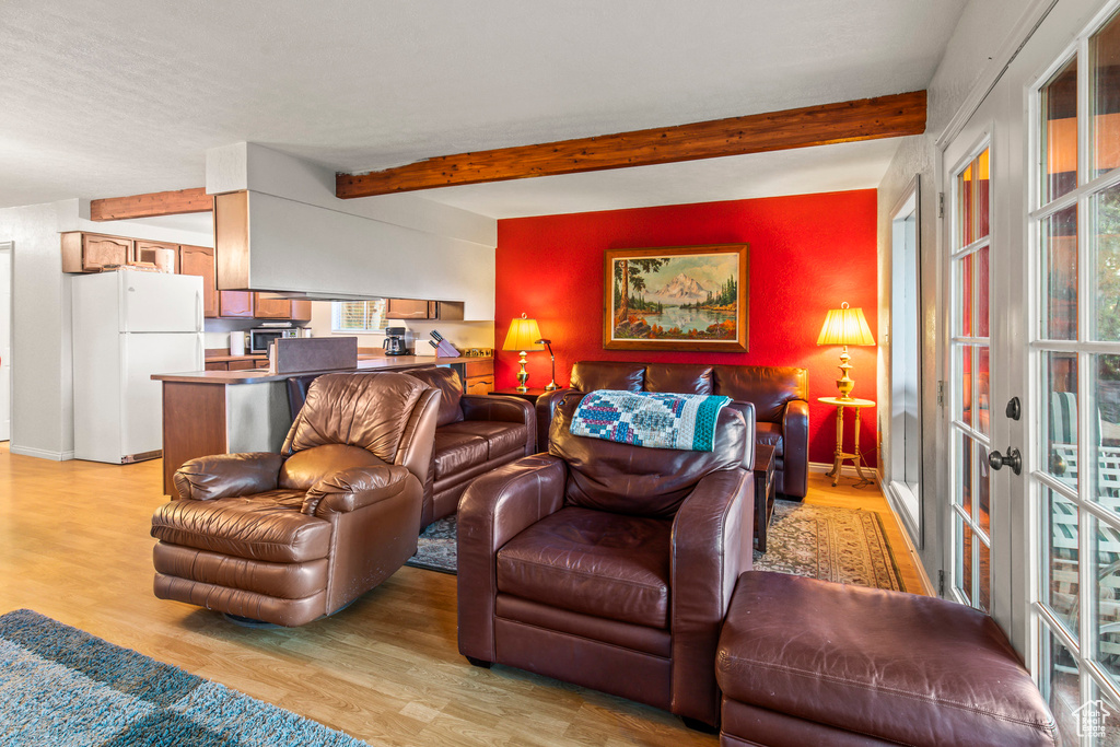 Living room with light wood-style floors, healthy amount of natural light, beamed ceiling, and french doors