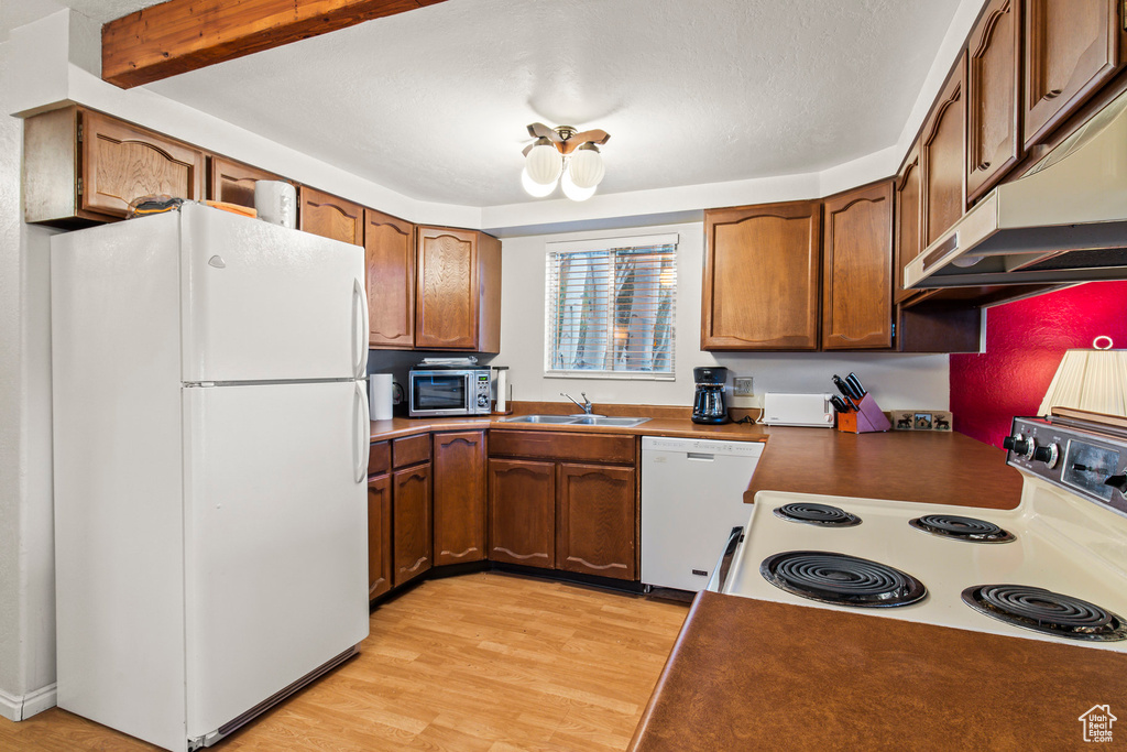 Kitchen with white appliances, under cabinet range hood, light wood-style floors, and brown cabinets