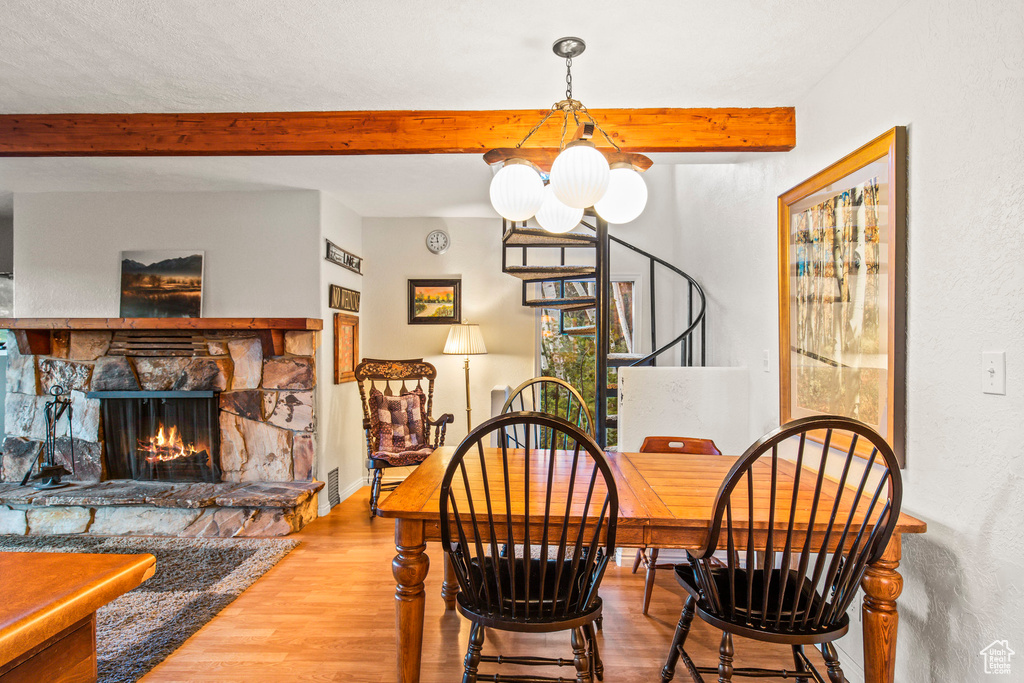 Dining room featuring beam ceiling, stairs, wood finished floors, a stone fireplace, and a chandelier