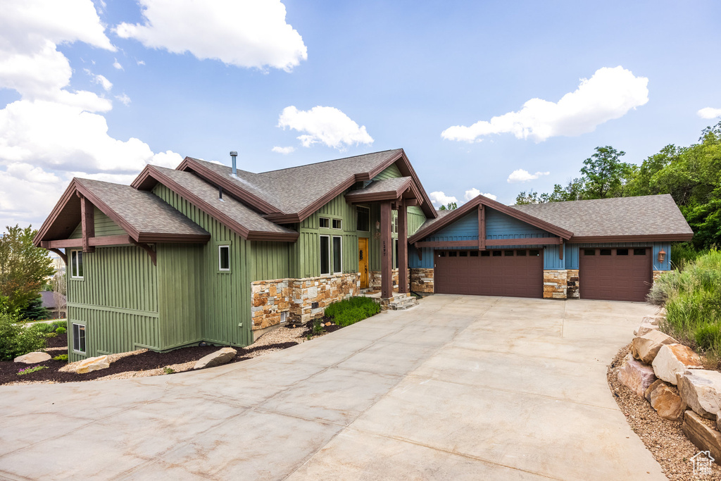 Craftsman inspired home featuring roof with shingles, concrete driveway, stone siding, and an attached garage