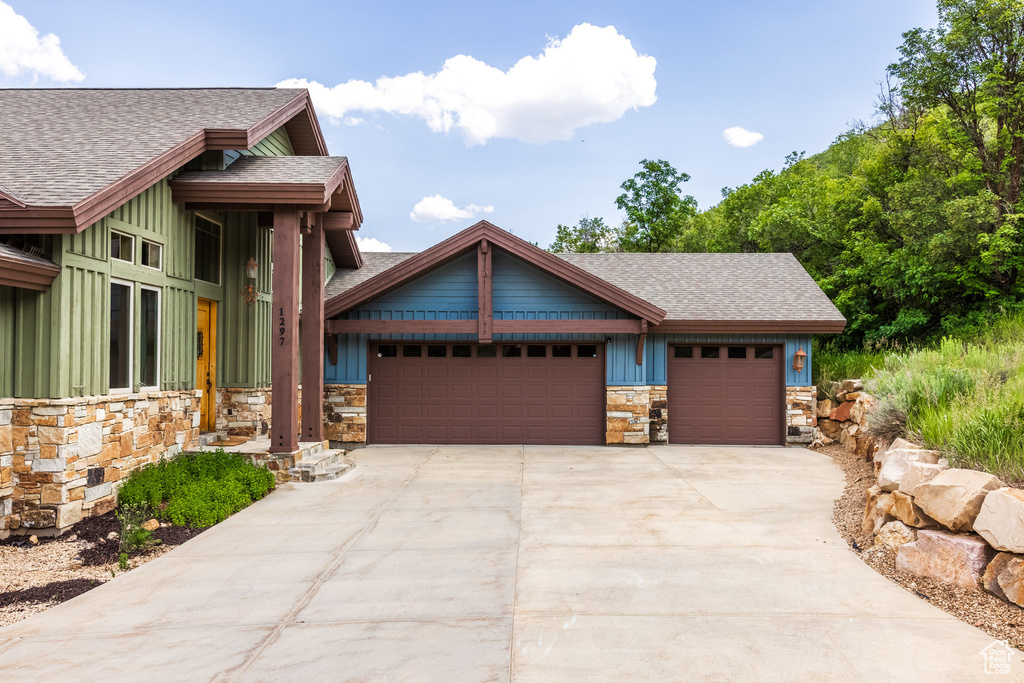 View of front facade with roof with shingles, board and batten siding, and stone siding
