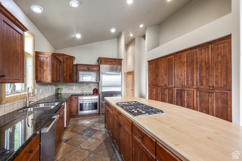Kitchen with appliances with stainless steel finishes, decorative backsplash, recessed lighting, lofted ceiling, and dark stone countertops
