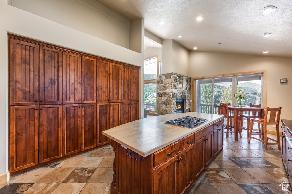 Kitchen featuring stainless steel gas cooktop, stone tile floors, a textured ceiling, a fireplace, and recessed lighting