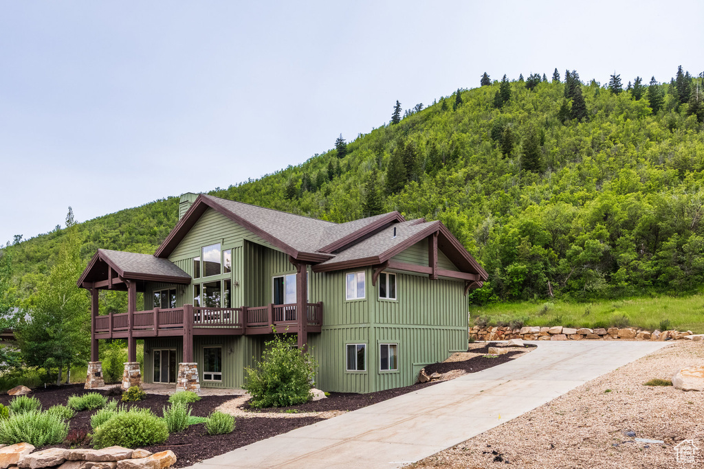 Rear view of house with a shingled roof, a deck with mountain view, and a view of trees