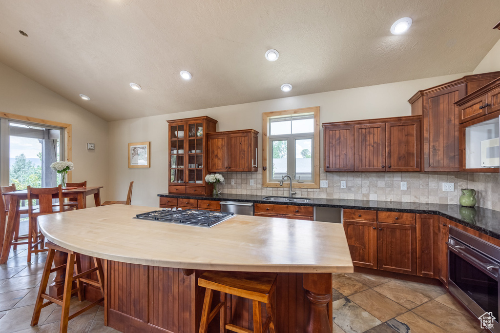 Kitchen with stainless steel appliances, decorative backsplash, a kitchen breakfast bar, lofted ceiling, and recessed lighting